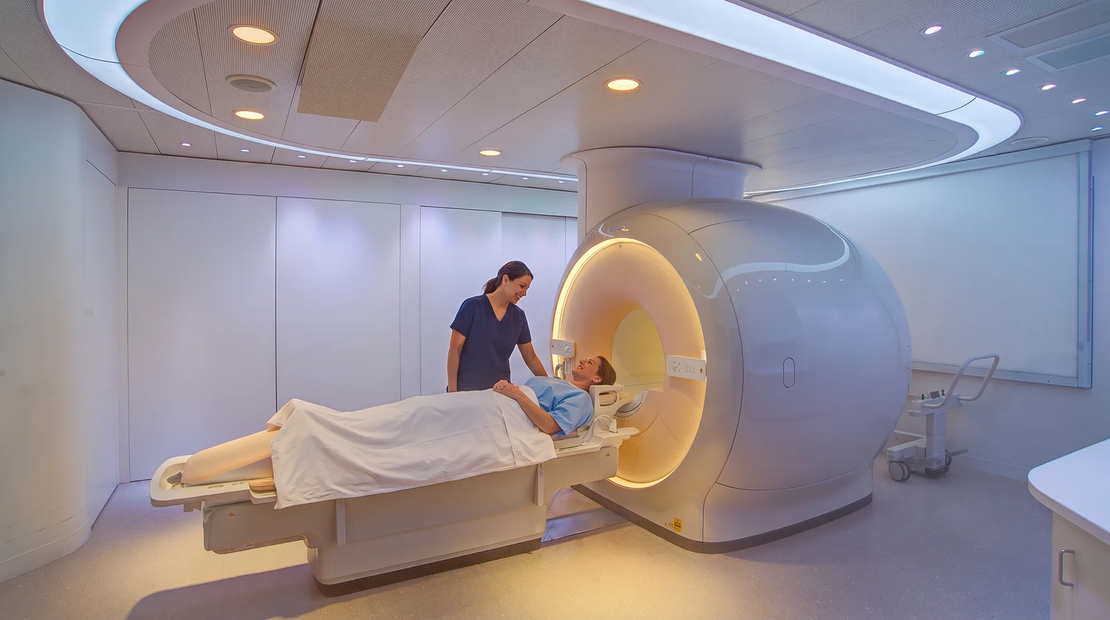A technologist talking with a patient lying on an MRI scanner table